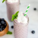 Overhead view of blueberry milkshake topped with whipped cream and mint.