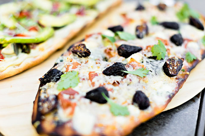 Flatbread pizza topped with cheese, tomato sauce, sliced figs, and herbs.
