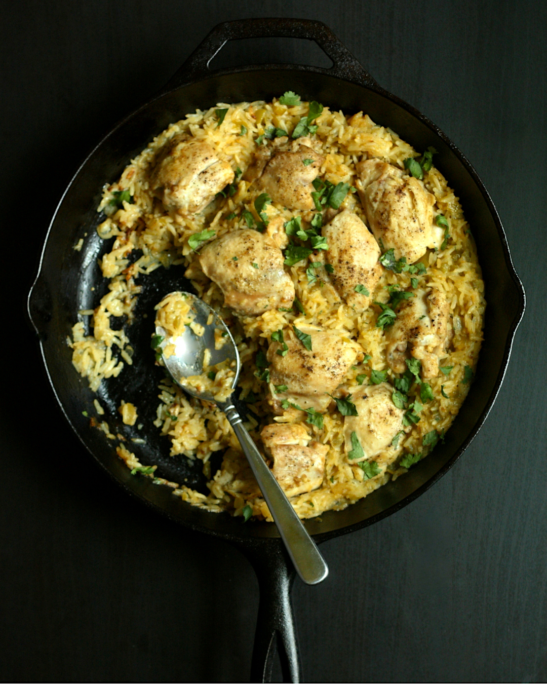 Arroz con Pollo Verde in a cast iron skillet with a silver serving spoon.