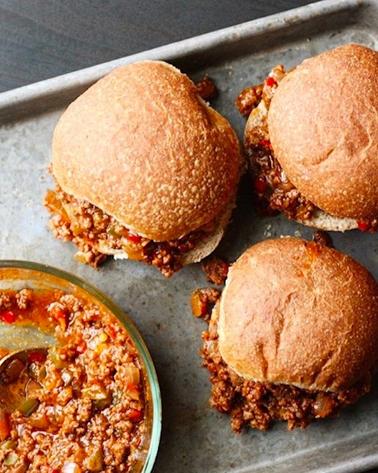 Sloppy Joes on a baking sheet next to a bowl of sloppy joe mix.