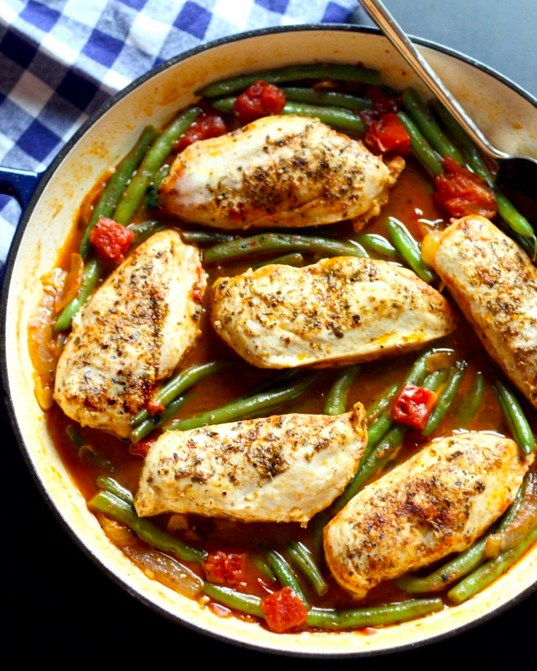 Greek chicken in a skillet with green beans, tomatoes, onions, and a light sauce.