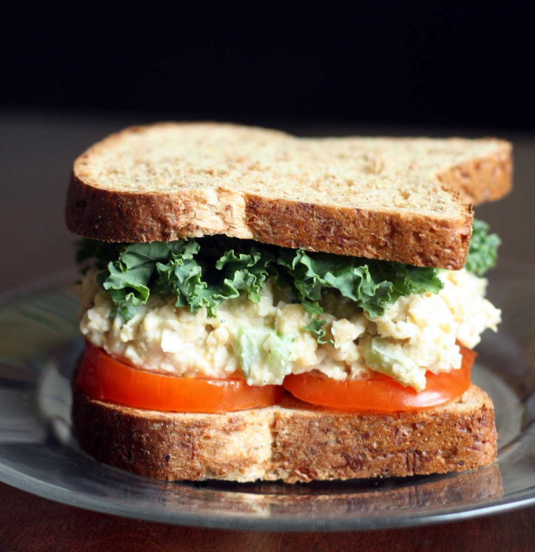 Sandwich with vegan chickpea salad topped with tomato and lettuce.
