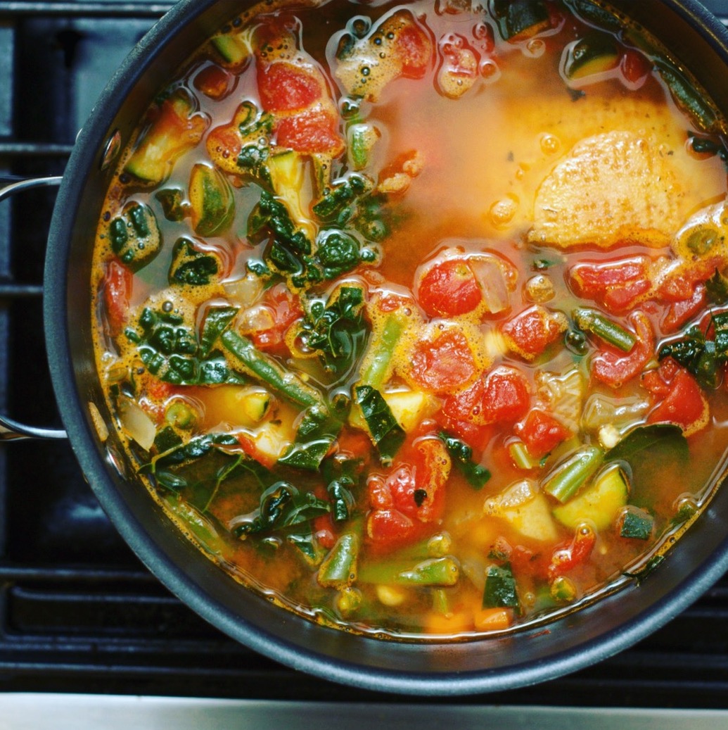 Minestrone soup with tomatoes, spinach, and green beans in a pot on the stove.