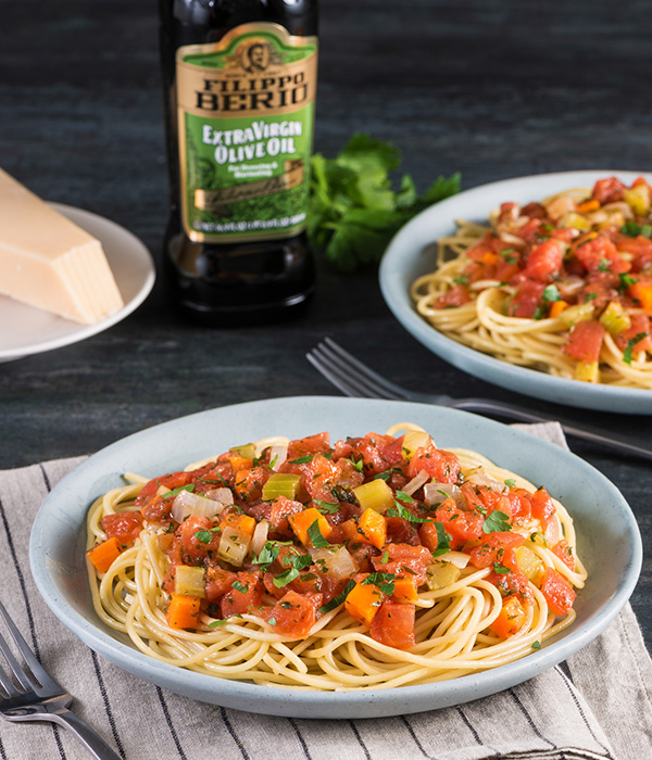 Pasta topped with tomatoes and veggies served in a dish.
