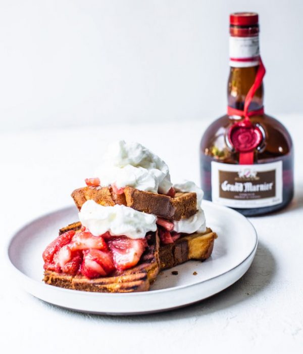 Grilled pound cake topped with strawberries and whipped cream on a plate in front of a bottle of Grand Marnier.