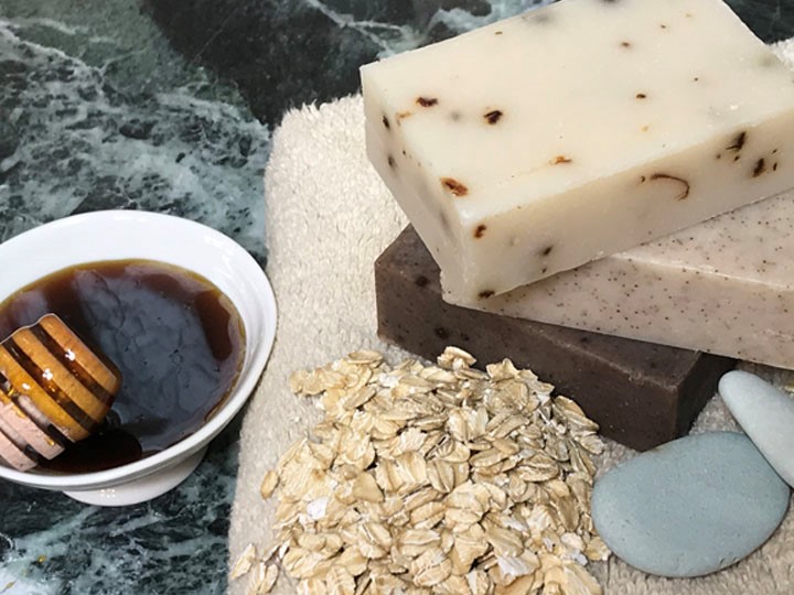 Marble counter with a towel topped with oats and handmade soap blocks next to a dish with honey.