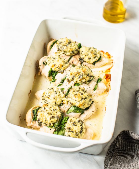 Baking dish with chicken breasts topped with spinach and mozzarella and cream cheese mixture.