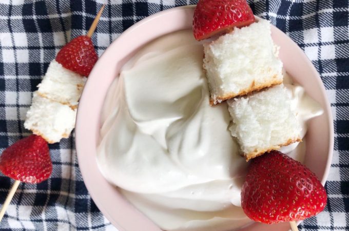Bowl with creamy whipped cream topped with a skewer of angel food cake and strawberries.