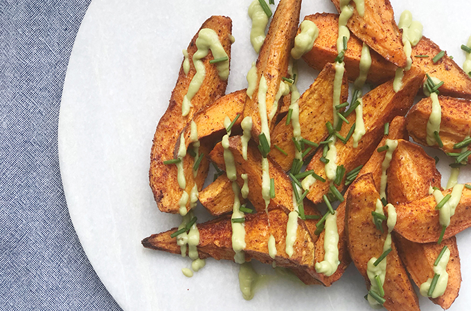 Plate with potato wedges drizzled with an avocado cream sauce.