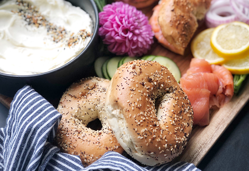 Platter with everything bagels, cream cheese, salmon, sliced cucumbers, red onion and sliced lemons.