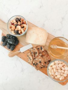 Cheese board with blackberries, nut mix, honey, cheese and multigrain crackers.