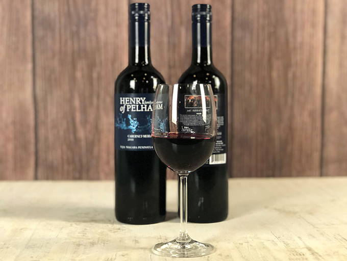 Bottles of Henery of Pelham red wine behind a glass of wine.