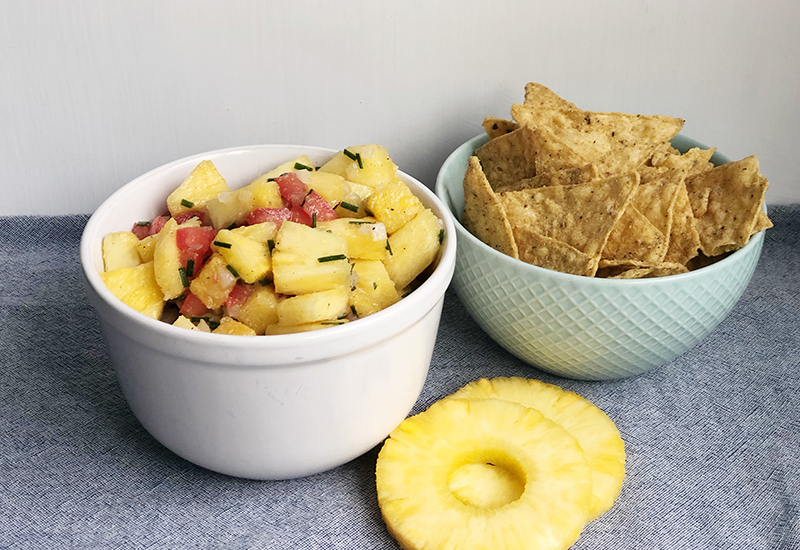 Bowl with a pineapple salsa with tomatoes next to a bowl of tortilla chips.