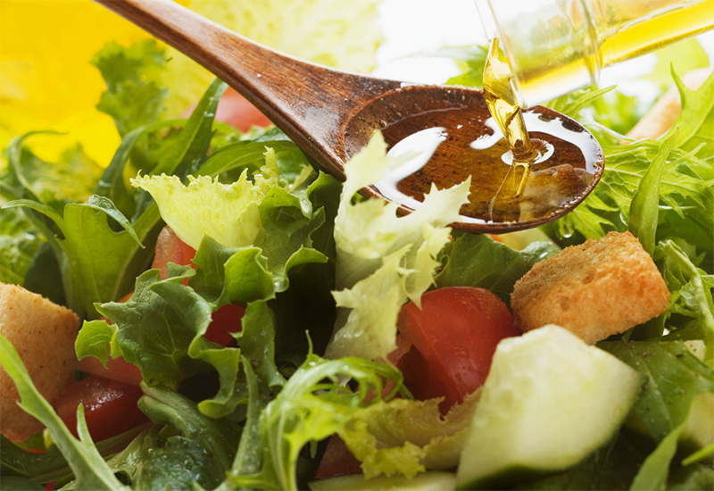 Salad with cucumber, tomato and croutons with olive oil being poured on a wooden spoon.