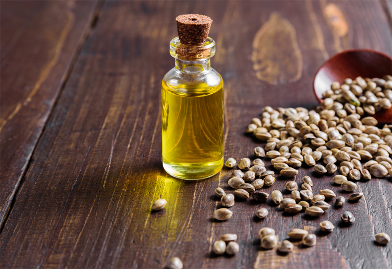 Small bottle with a yellow oil surrounded by hemp seeds.