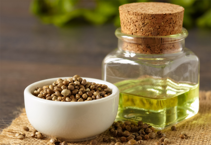 Jar with a pale green liquid next to a bow with hemp seeds.