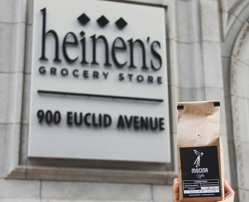 Bag of Mocina coffee grounds being held next to a Heinen's Grocery Store sign.