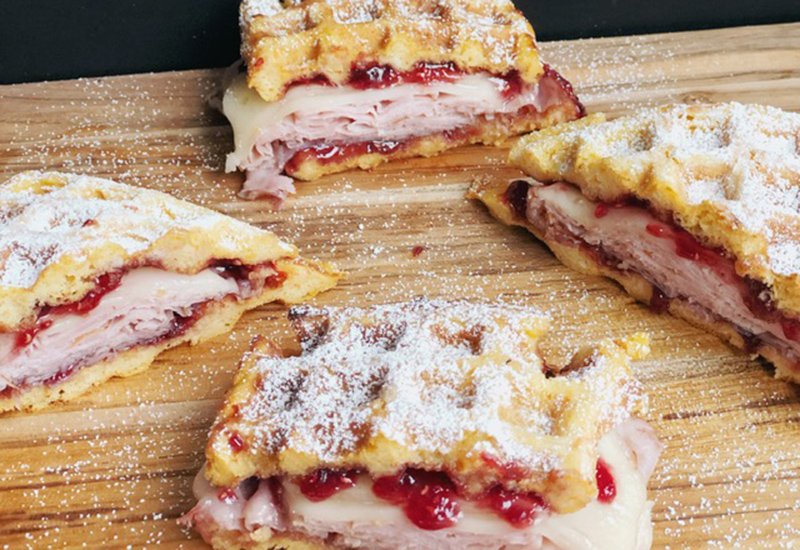 Waffle sandwich with Swiss cheese, ham slices and raspberry jam topped with powdered sugar.