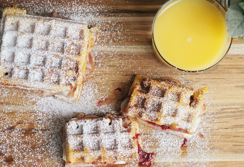 Peanut butter and jelly stuffed waffles, dusted with powdered sugar on a cutting board with orange juice.