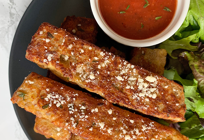 Savory multigrain-parmesan French toast sticks with a side of marinara and bed of lettuce.