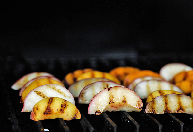 Stone fruit slices being cooked on a grill.