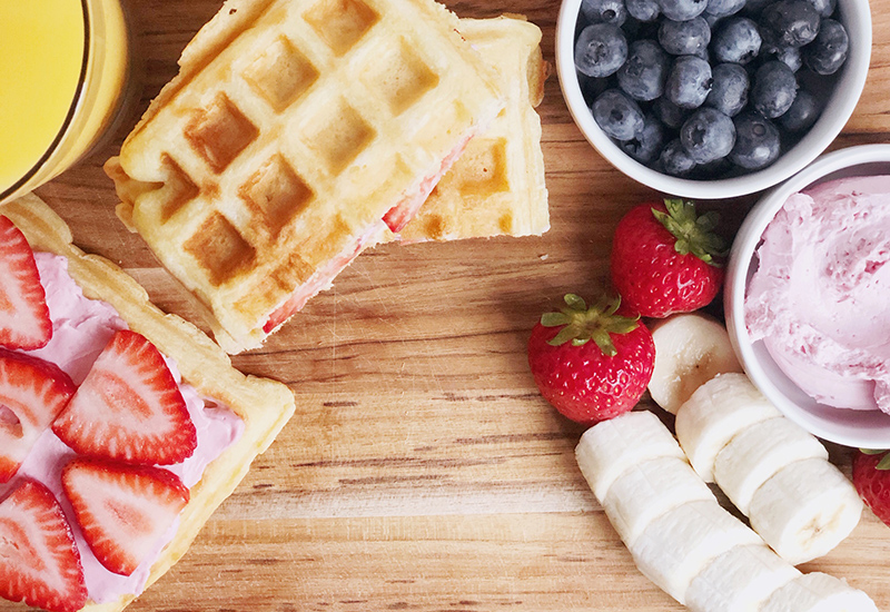 Waffles stuffed with a strawberry cream cheese and sliced strawberries next to blueberries, strawberries, and sliced bananas.