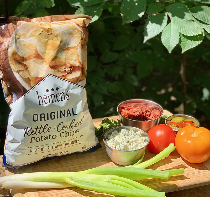 Heinen's original kettle cooked potato chips on a cutting board with chives, tomatoes, bacon, relish and cheese.
