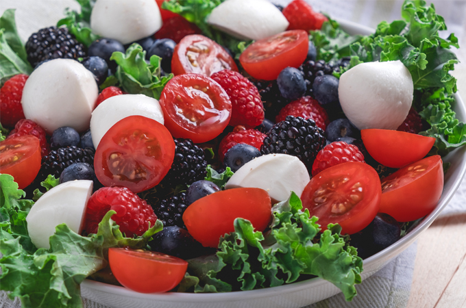 Salad with lettuce, mozzarella balls, blueberries, blackberries, and sliced cherry tomatoes.