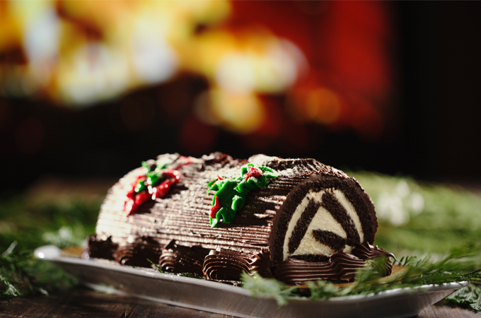 Holiday Yule Log cake topped with chocolate icing and decorative iced leaves and berries.