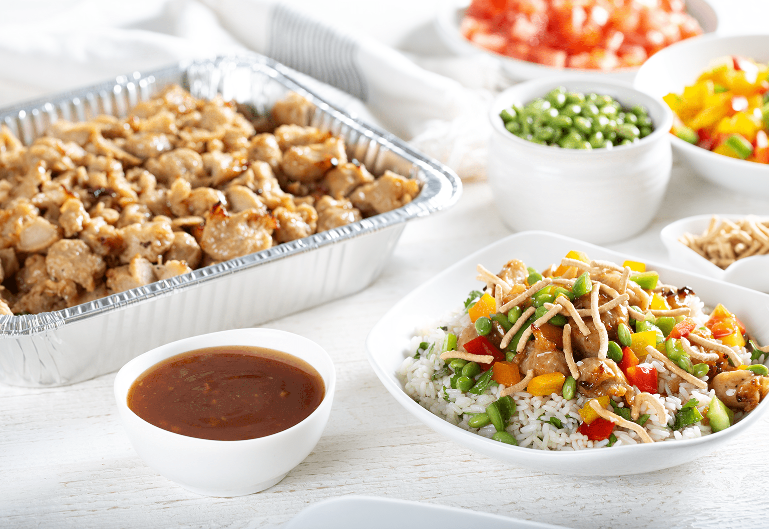 A Grilled Chicken Bowl Beside Bowls and Pans of Chicken, Fresh Vegetables and Sauces