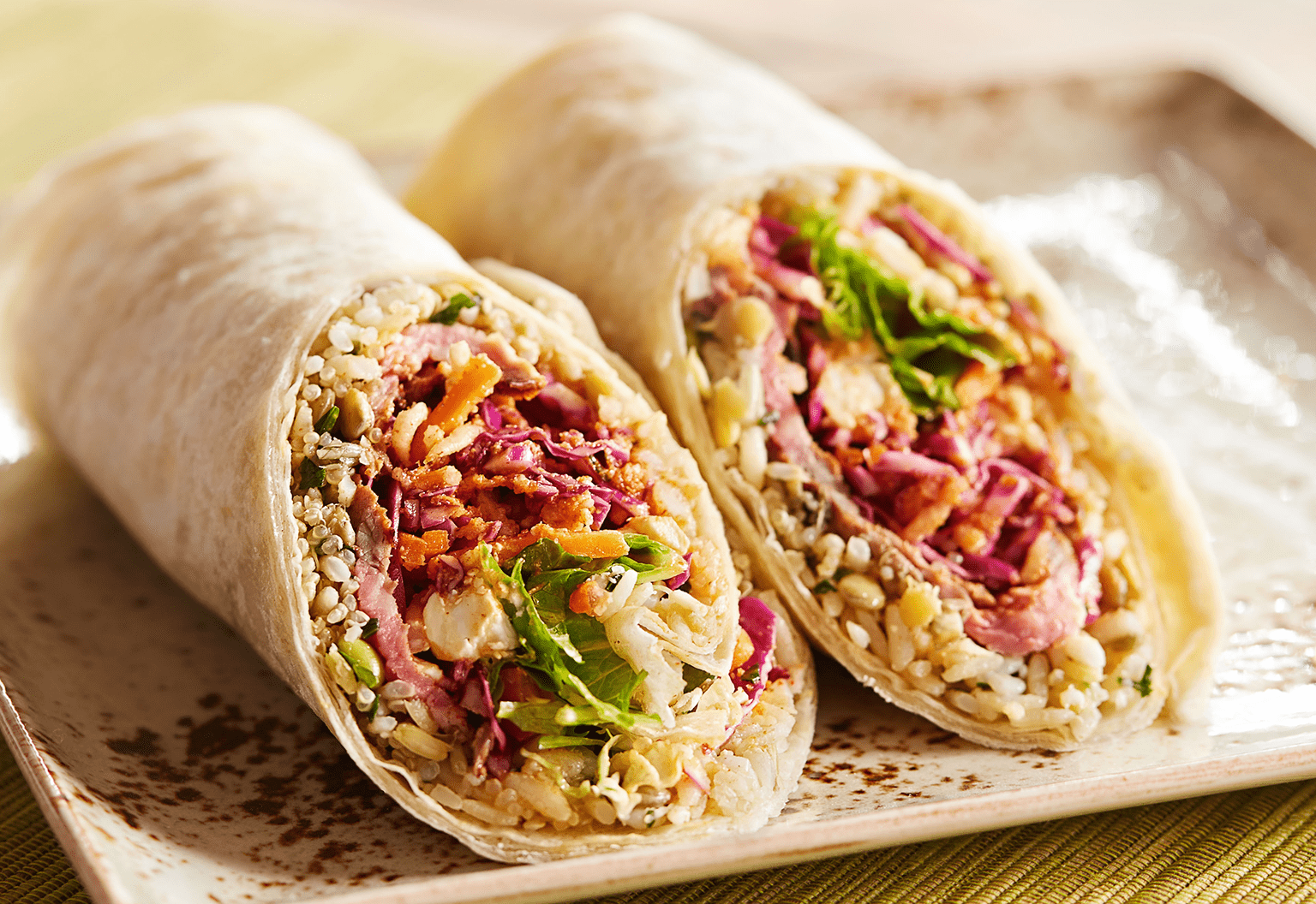 A Rice and Veggie Filled Wrap Sliced in a Half on a Plate.