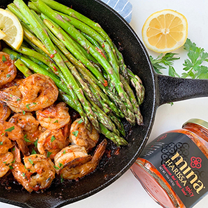 Skillet with spicy harissa-seasoned shrimp and asparagus with slices of lemon.