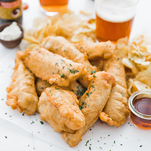 Fried fish on a plate with fries and a small dish with vinegar.