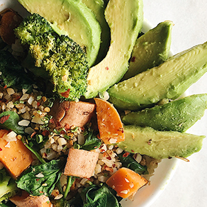 Bowl with grains topped with sliced avocados, spinach, sweet potatoes cubes and broccoli florets.