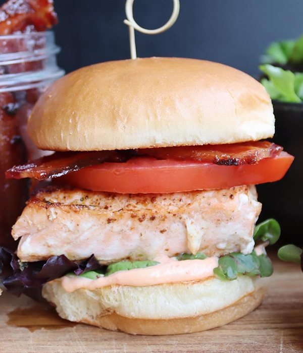 Burger with bacon, tomato, salmon, lettuce, and a creamy sauce.