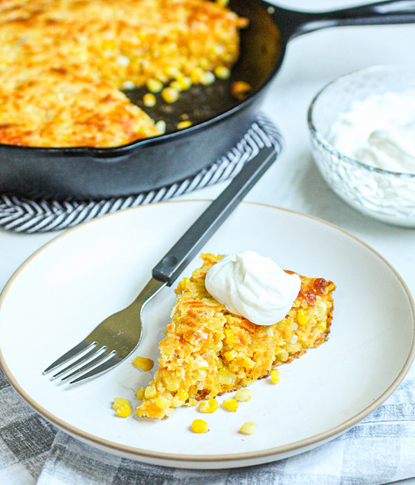 Plate with a slice of sweet corn fritter pie topped with sour cream.