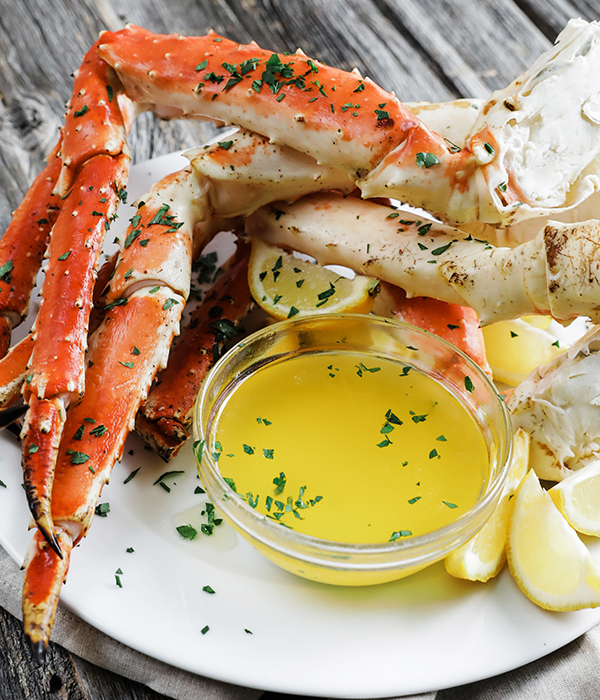 Fresh crab leg clusters topped with herbs with a side of melted butter and sliced lemons.