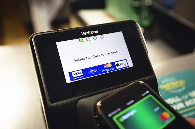 View of a payment kiosk with a phone tapping it for contactless payment.
