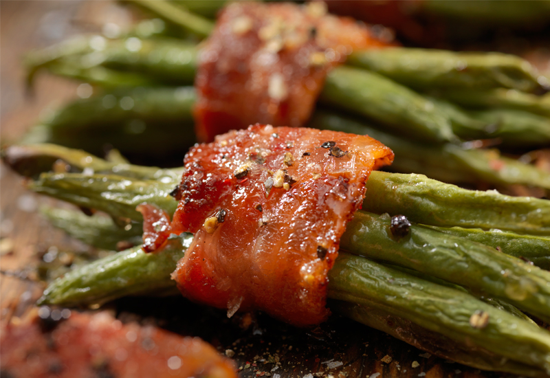 Breen bean bundles wrapped in bacon on a cutting board.
