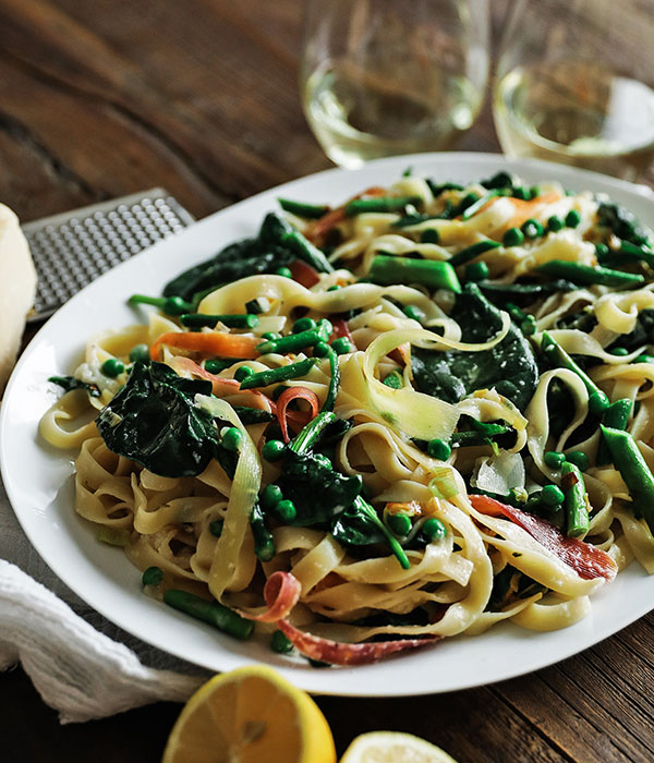 Linguine pasta with spinach, asparagus, and thinly sliced carrots served with glasses of white wine.