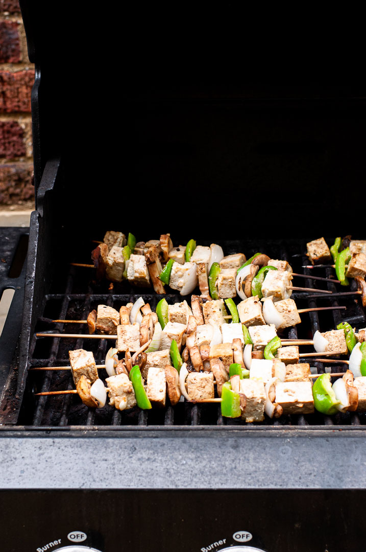 Skewers with mushrooms, tofu, bell pepper, and onions on an open grill.