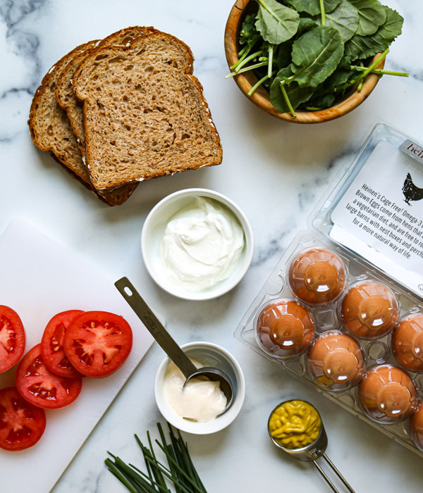 Classic Egg Salad ingredients including bread, spinach, tomato, mayonnaise, mustard, and eggs.