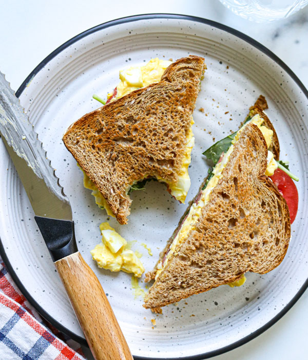 Heinen's Classic Egg Salad on a sandwich with lettuce and tomato, cut diagonally.