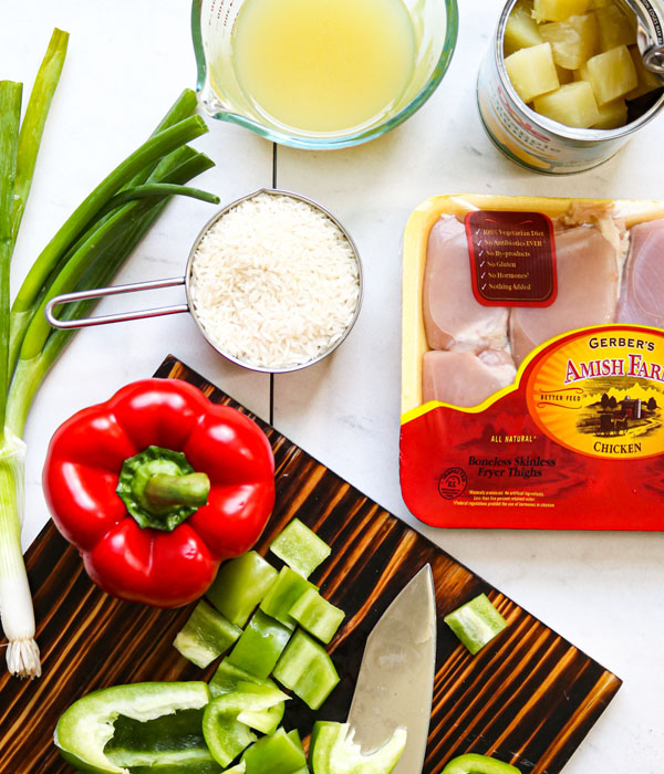 Diced bell peppers on a cutting board next to rice, pineapple, green onion, and chicken thighs.