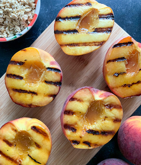 Pitted peaches sliced in half with charred grill marks on a cutting board.