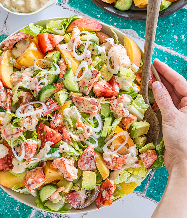 Lobster Heirloom Tomato Salad in a serving bowl with a wooden spoon.