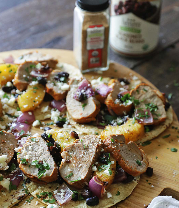 Corn tortilla shells topped with red onion, black beans, pineapple, and sliced pork tenderloin pieces.