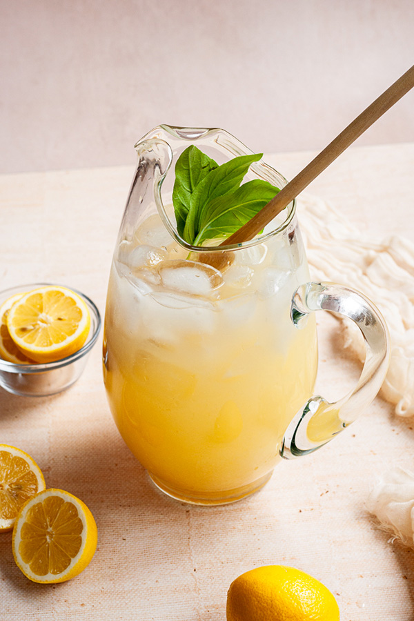 Pineapple lemonade in a pitcher with a wooden spoon surrounded by fresh cut lemons.