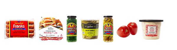 Spread of Chicago Dog ingredients including hot dogs, hot dog buns, relish, pickles, tomatoes, peppers, and potato salad.