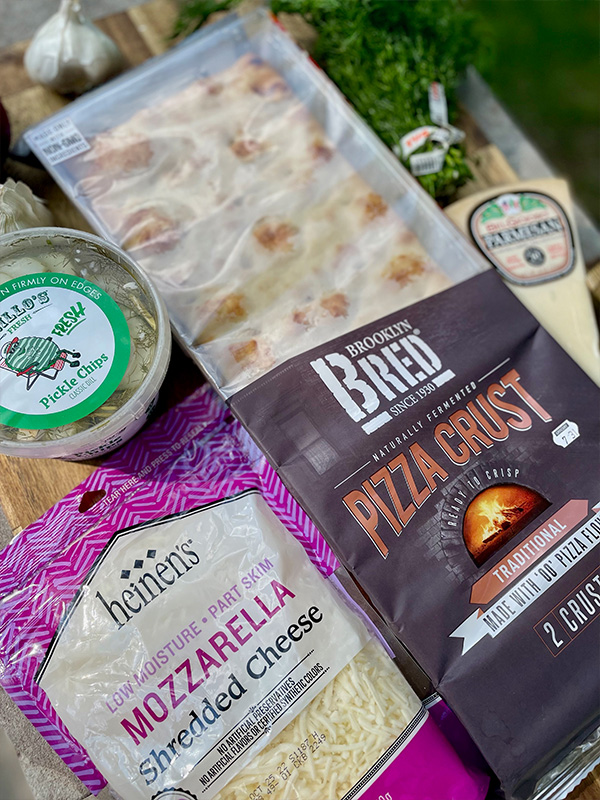 Cutting board with Brooklyn Bred flatbread pizza crust, Heinen's mozzarella cheese, Grillo's pickle chips and parmigiano Reggiano cheese.